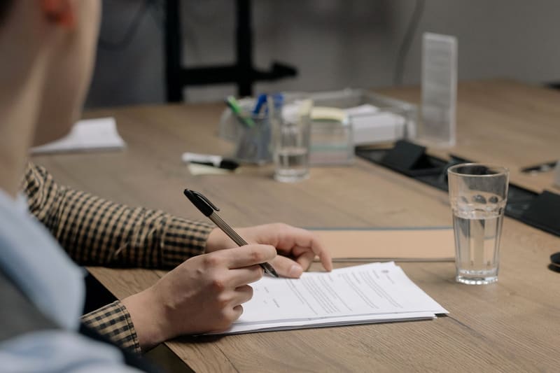 A person reviewing and signing documents at a wooden desk