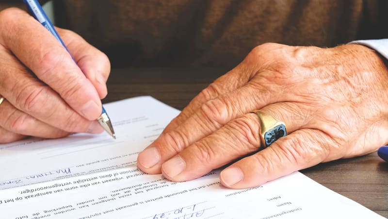 An older person's hands signing a document at a desk